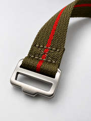 An olive green woven watch strap with a red stripe and a brushed silver steel buckle designed for tool watches and field watches alike. 