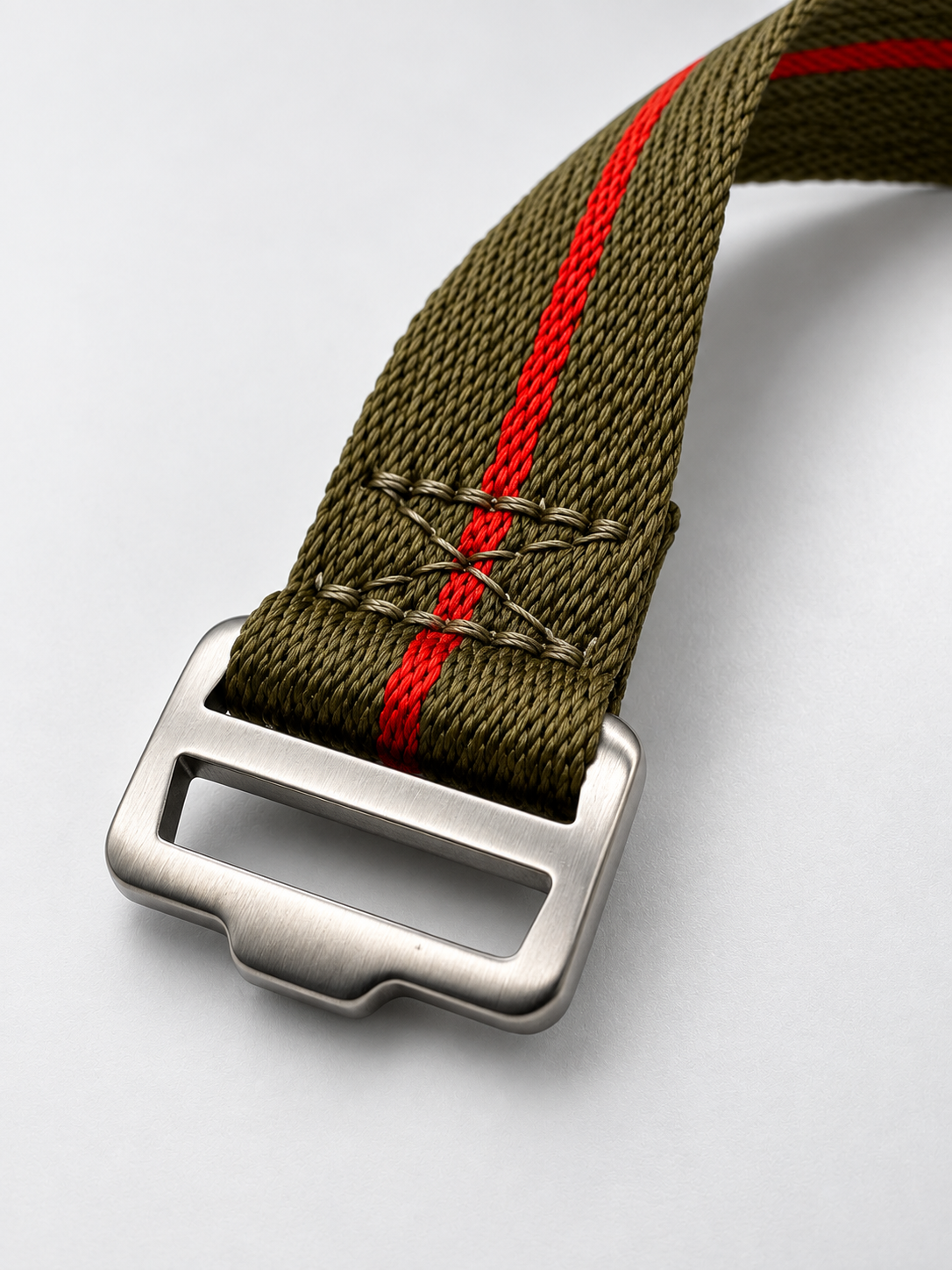 An olive green woven watch strap with a red stripe and a brushed silver steel buckle designed for tool watches and field watches alike. 